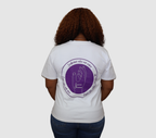 Woman wearing a white t-shirt with a purple graphic design on the back, standing against a gray background.