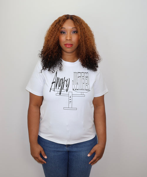 Woman wearing a white t-shirt with black 'Angry but Justified' text and graphic design, standing against a gray wall