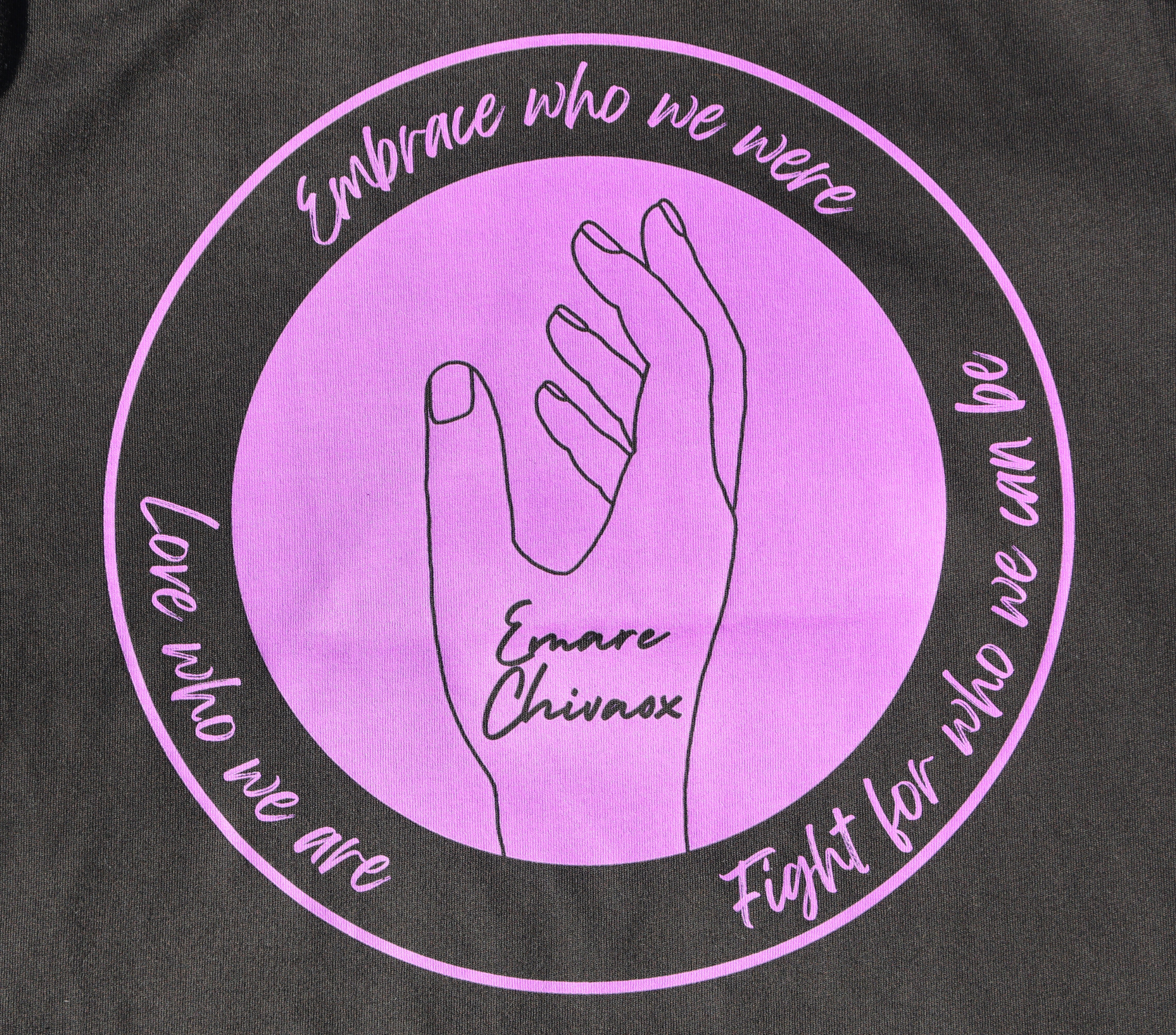 Zoomed in view of the back of a black t-shirt with a purple graphic design featuring the outline of a hand and text.