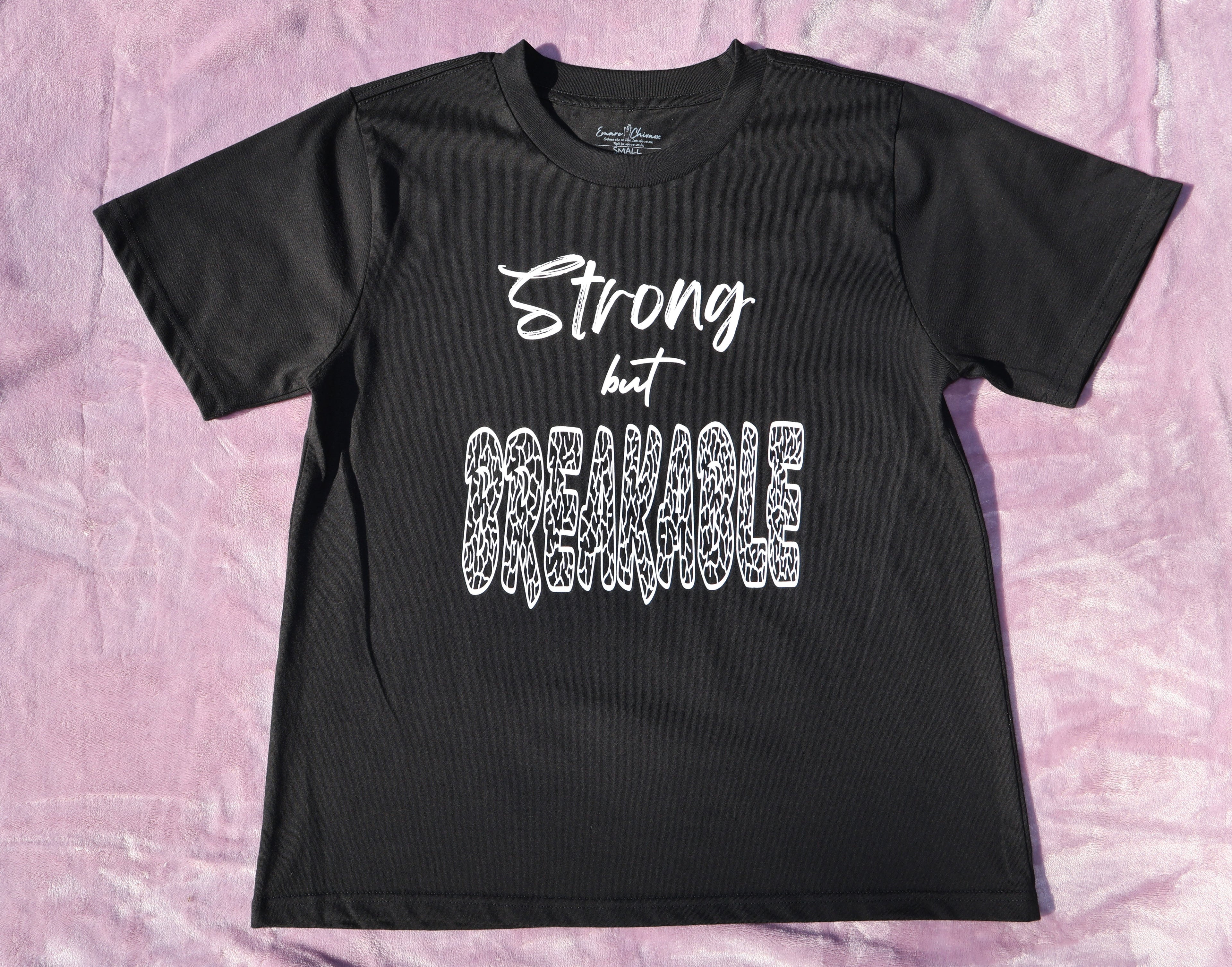 Black t-shirt with white 'Strong but Breakable' text and graphic design on a lavender background