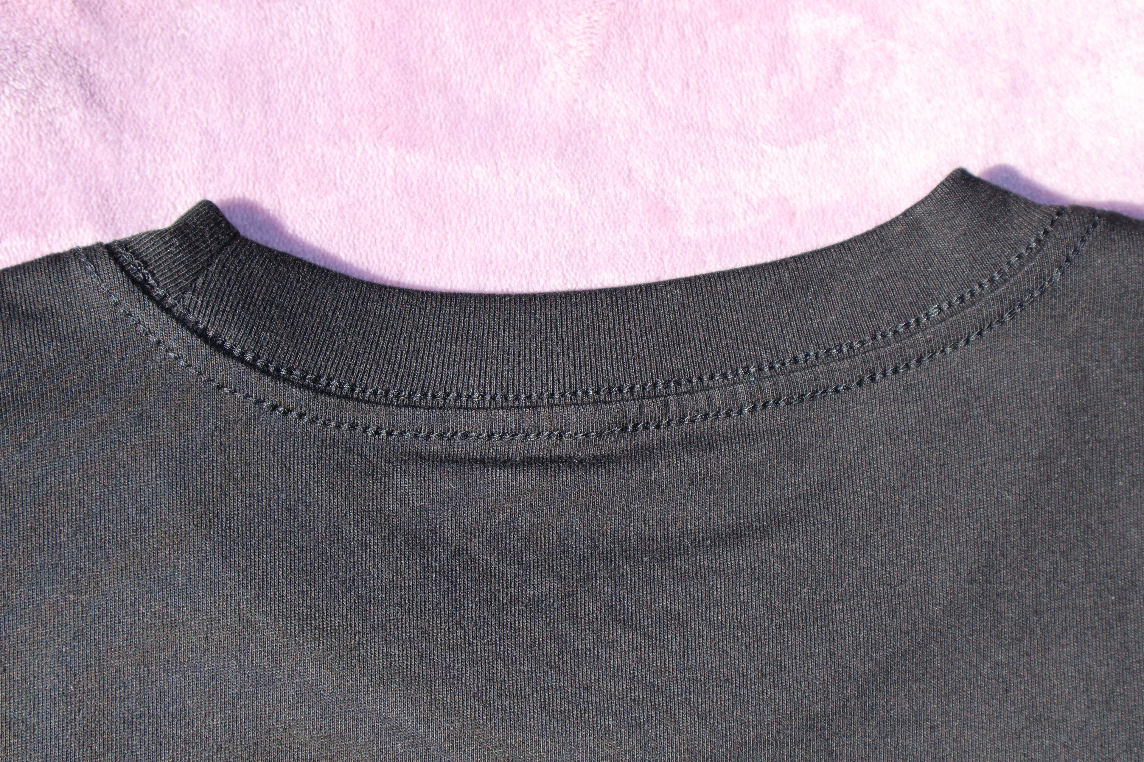 Close up of the back collar of a black t-shirt on a lavender background.