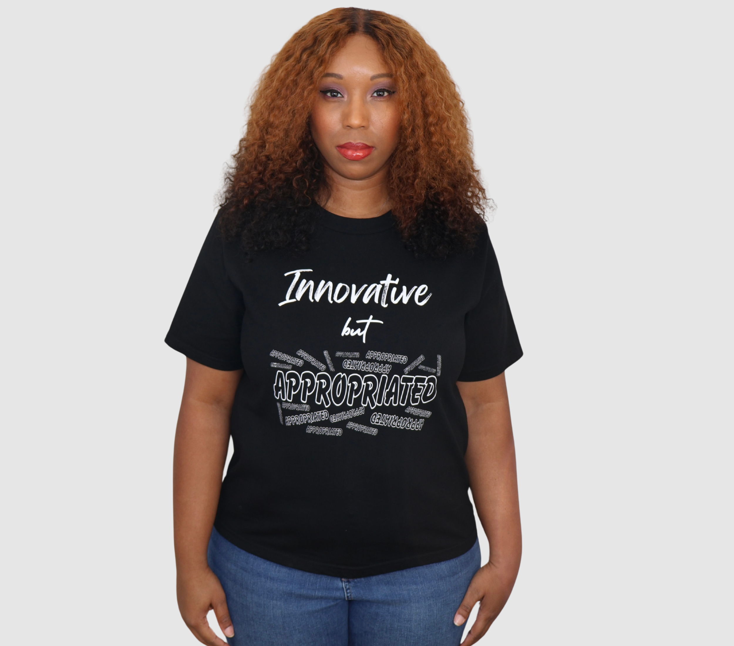 Woman wearing a black t-shirt with white 'Innovative but Appropriated' graphic design, standing against a gray background.