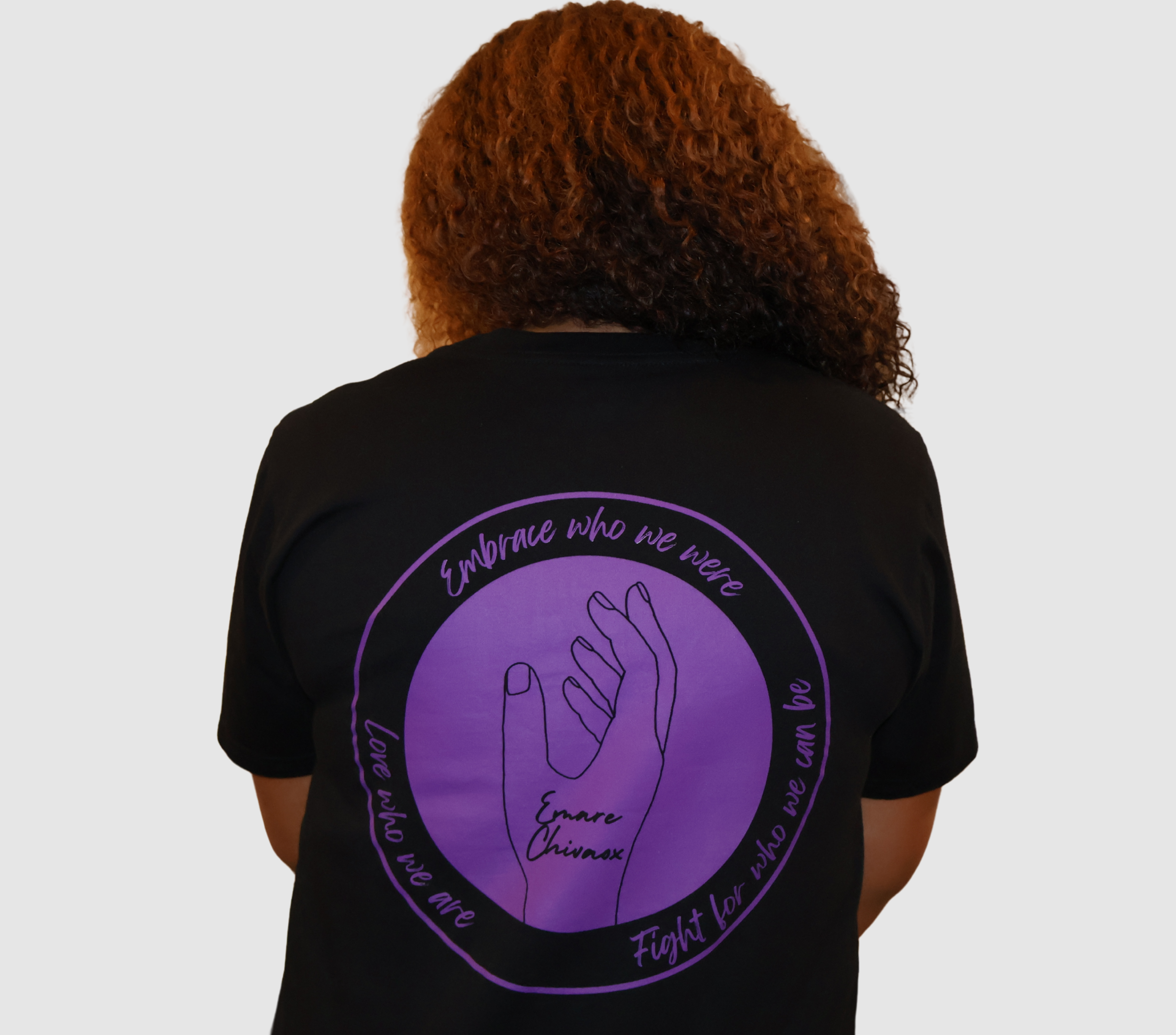 Woman wearing a black t-shirt with a purple graphic design on the back, standing against a gray background.