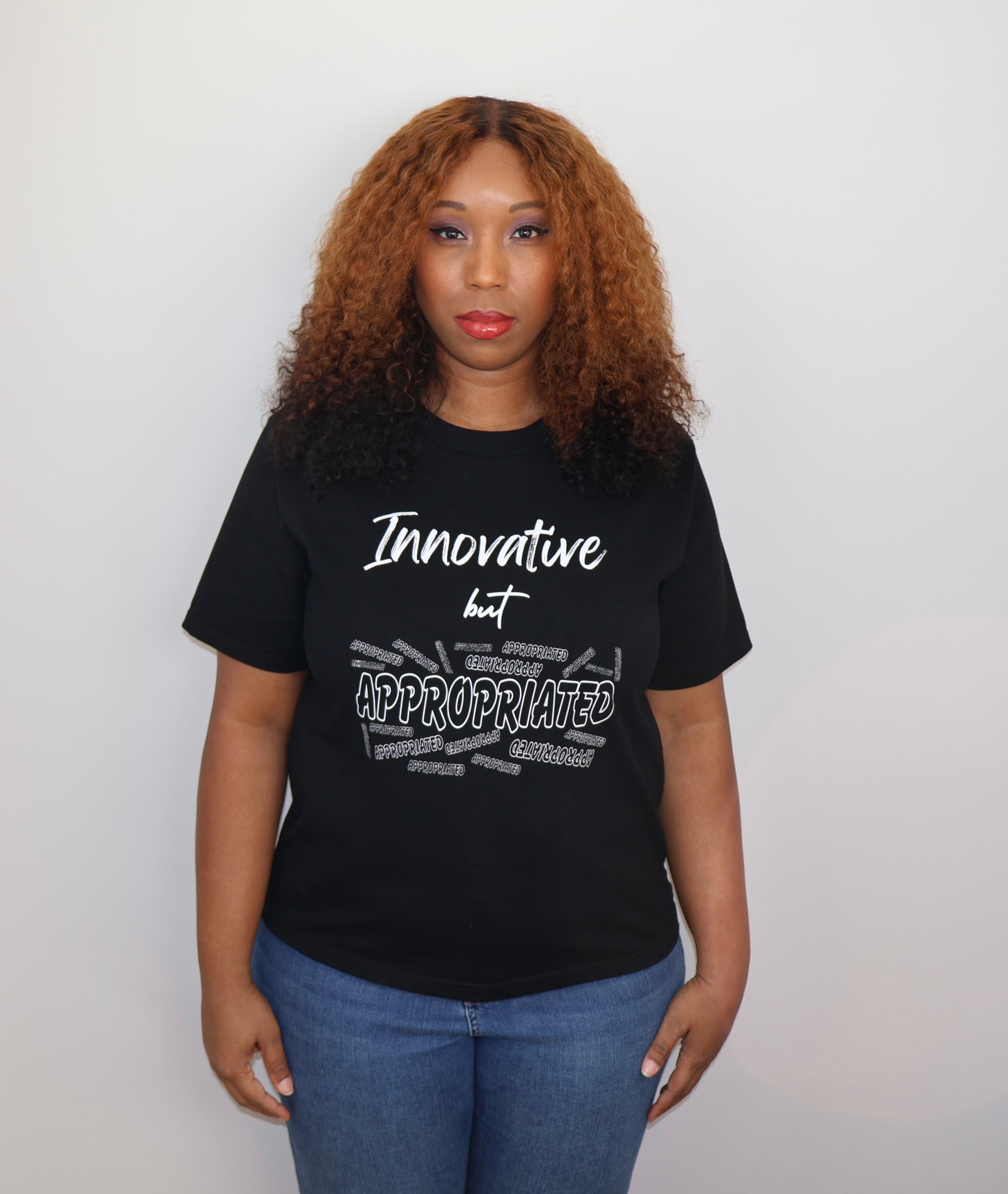 Woman wearing a black t-shirt with white 'Innovative but Appropriated' text and graphic design, standing against a gray wall