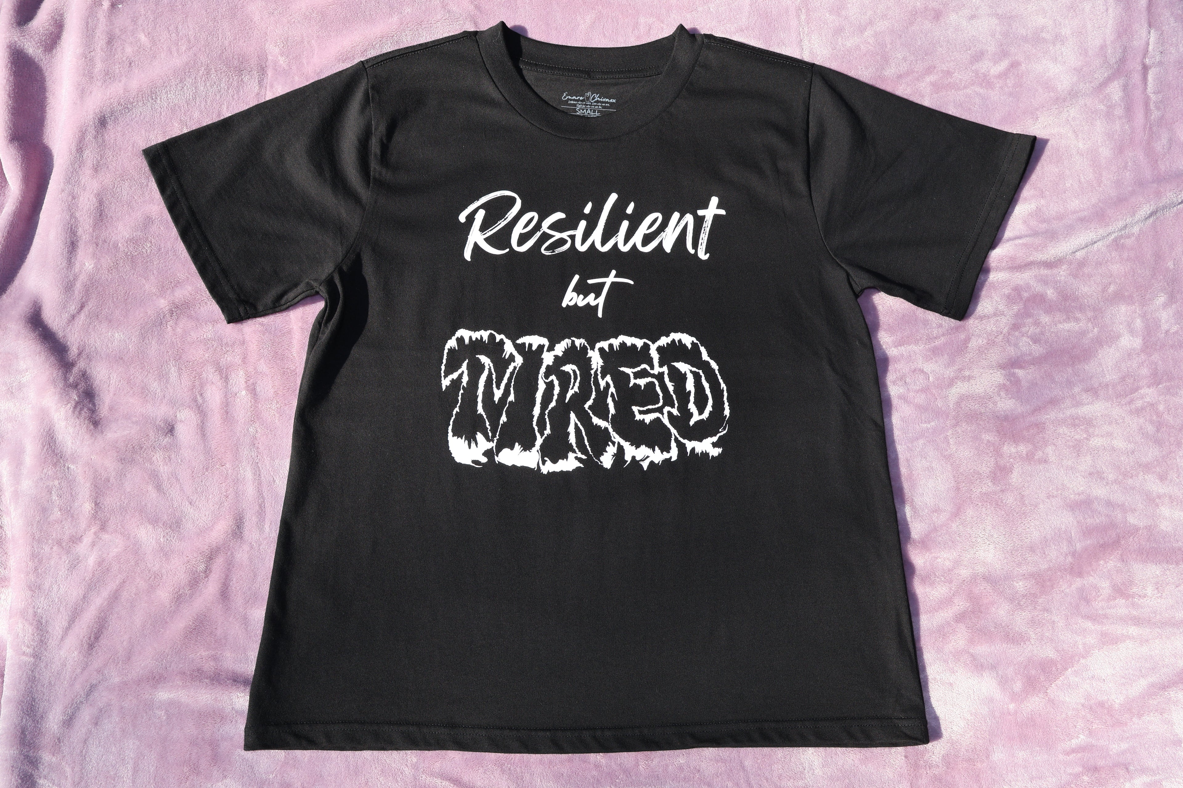 Black t-shirt with white 'Resilient but Tired' text and graphic design on a lavender background.