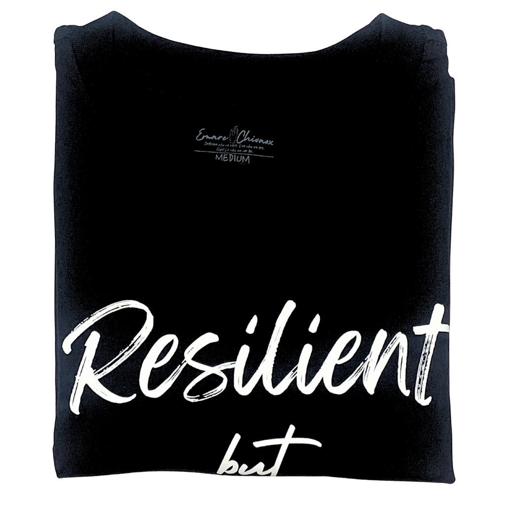 Front of black t-shirt folded with "Resilient but" white text design on a white background