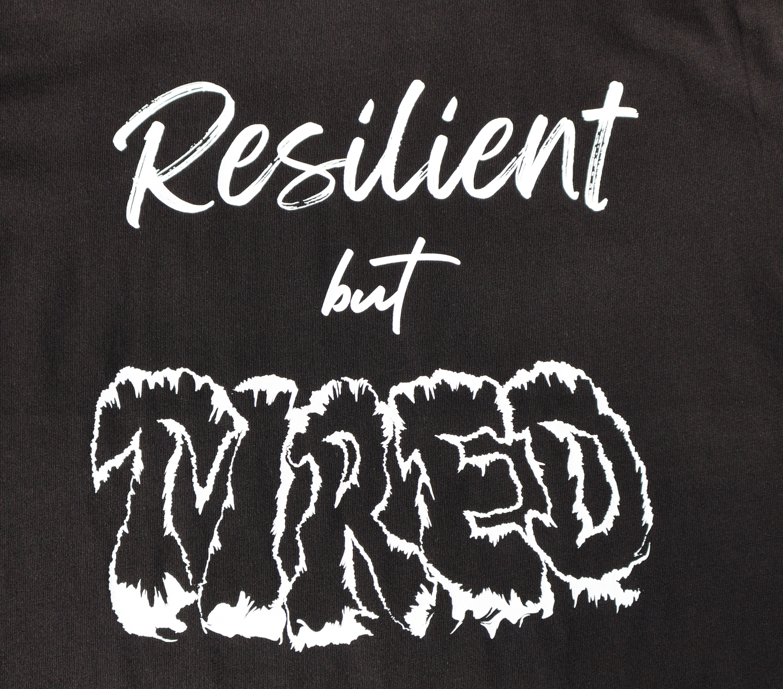 Zoomed in view of black t-shirt with white 'Resilient but Tired' graphic design.