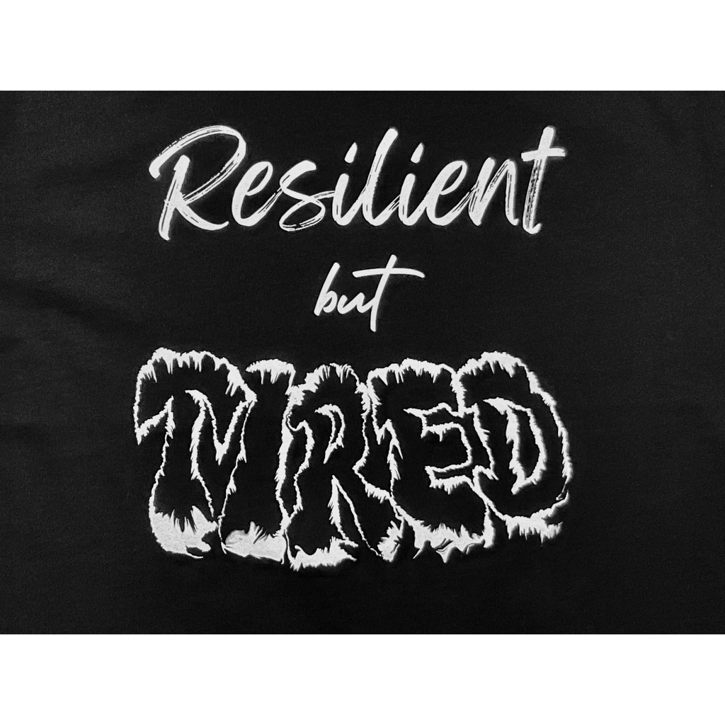 Center of black t-shirt with "Resilient but Tired" white text design on a white background