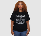 Woman wearing a black t-shirt with white 'Resilient but Tired' graphic design, standing against a gray background.