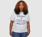 Woman wearing a white t-shirt with black 'Resilient but Tired' graphic design, standing against a gray background.