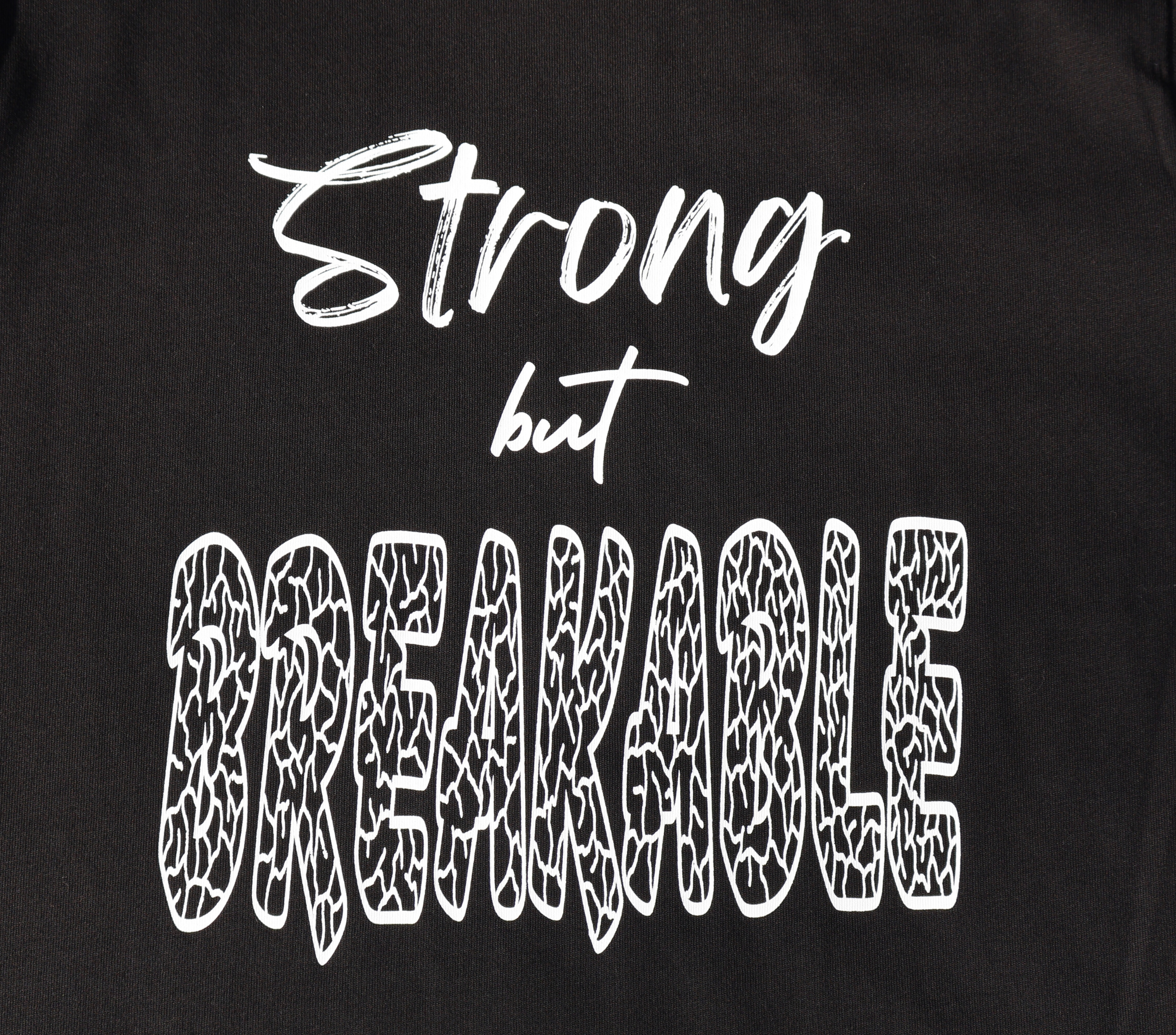 Zoomed in view of black t-shirt with white 'Strong but Breakable' graphic design.