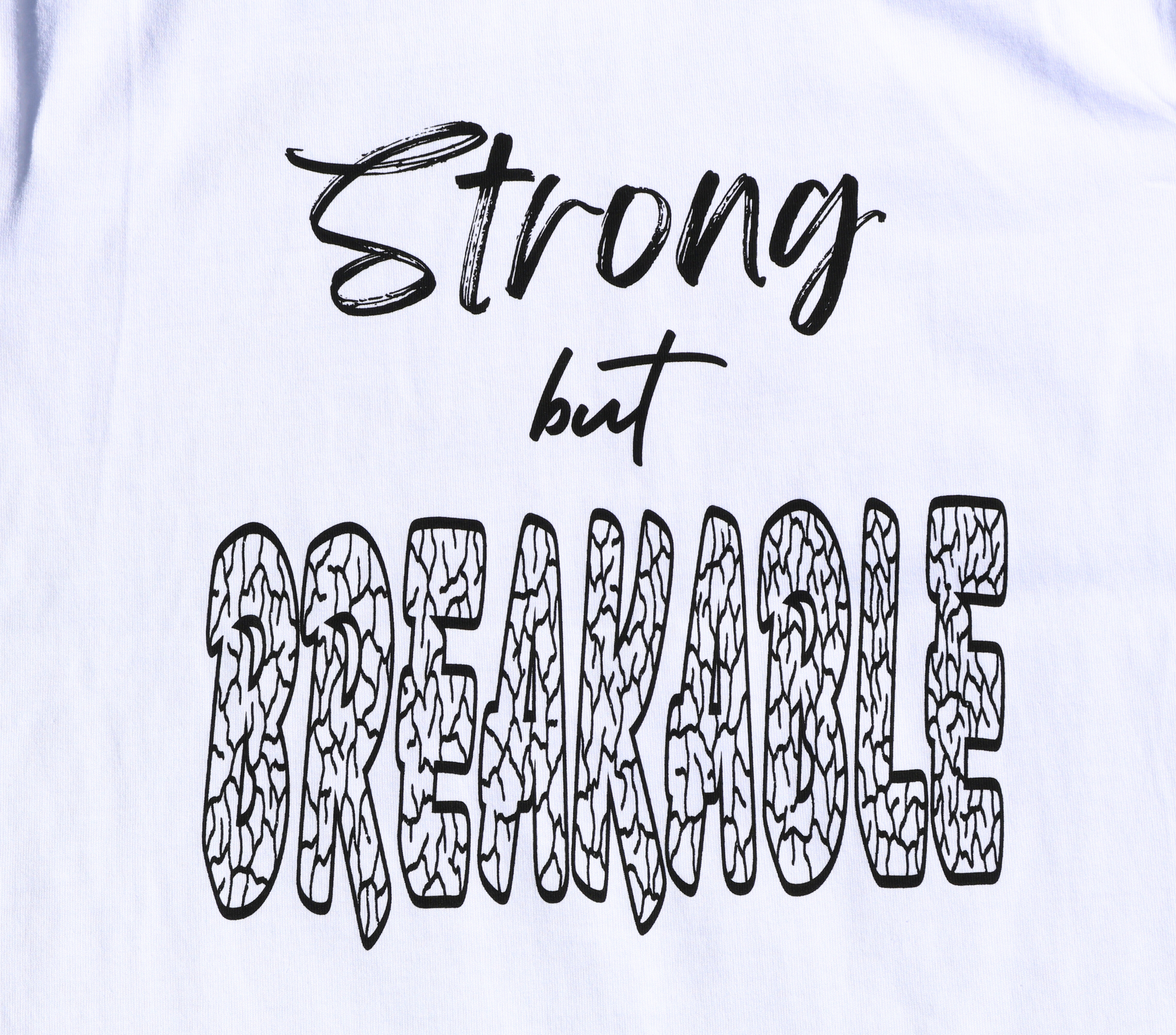 Zoomed in view of white t-shirt with black 'Strong but Breakable' graphic design.