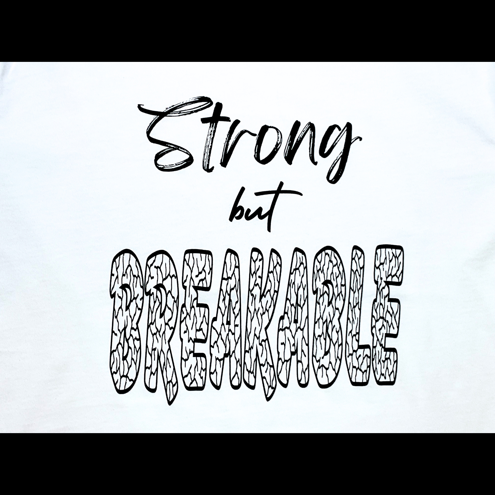 Center of white t-shirt with "Strong but Breakable" black text design on a black background