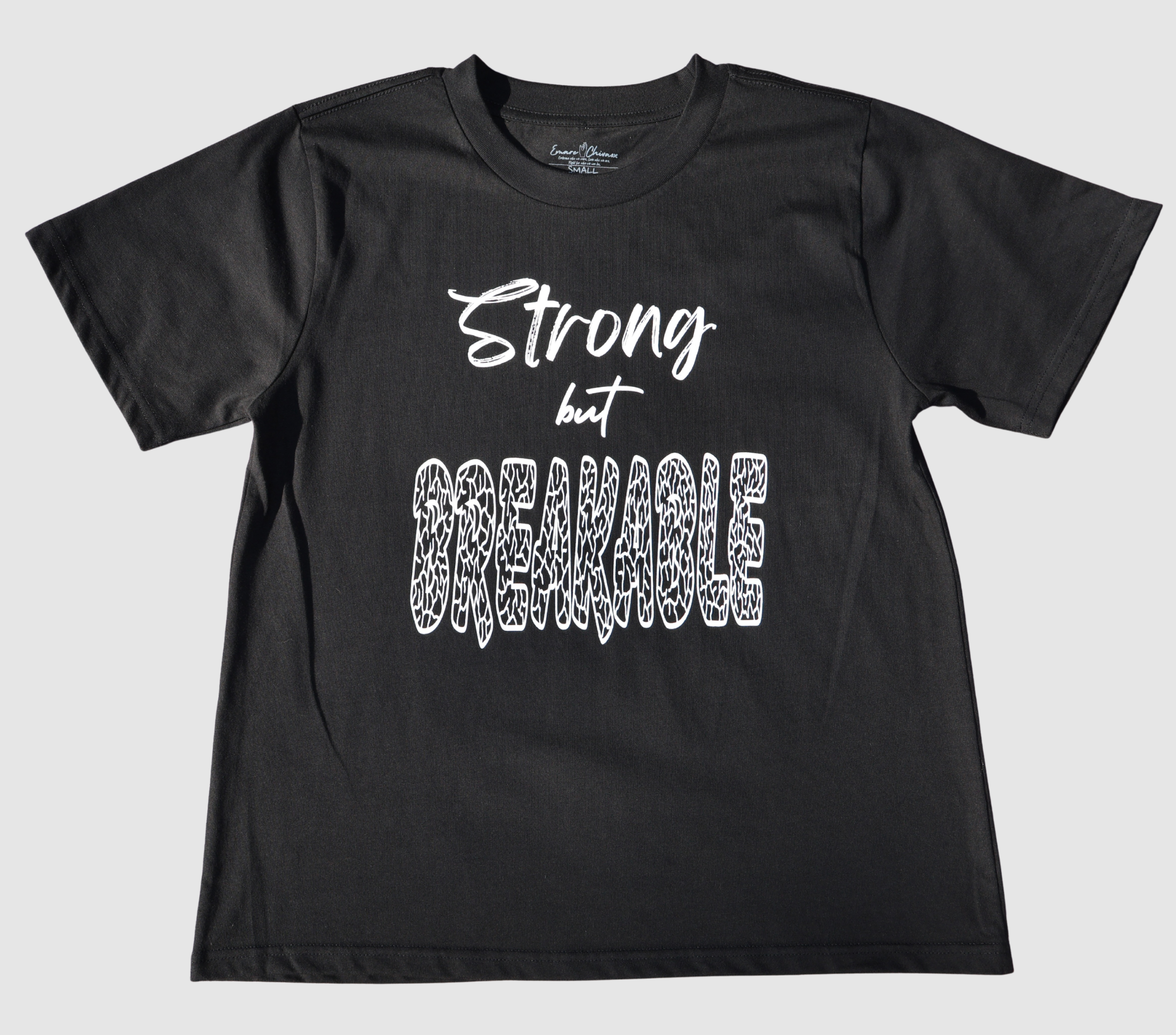 The front of a black t-shirt with white 'Strong but Breakable' graphic design on a gray background.